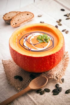 Delicious colourful orange pumpkin soup for the cold fall weather served in the hollowed out rind with scattered pumpkin seeds