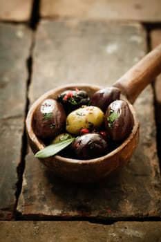 Piquant olives with a spicy chilli seasoning displayed in an old vintage wooden ladle or spoon on bricks with copyspace