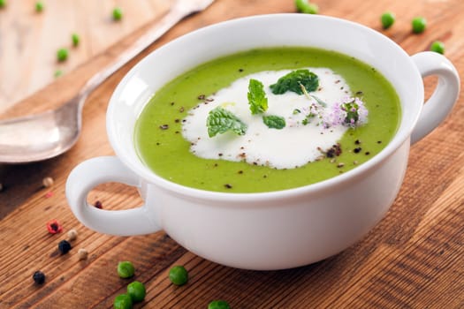 Bowl of healthy green pea soup topped with cream and fresh herbs served as a starter