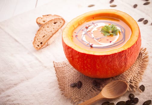 Colourful fall pumpkin soup served in the hollowed out gourd on a piece of rustic burlap with a wooden spoon
