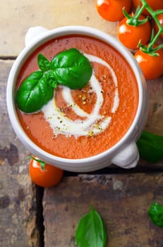 Overhead view of a bowl of tomato soup drizzled with cream and garnish with leaves of fresh green basil