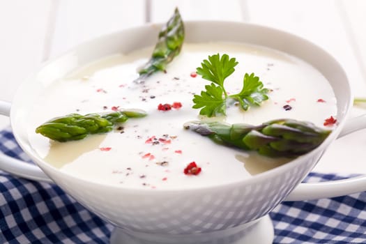 Closeup of fresh green asparagus tips in a bowl of cream of asparagus soup garnished with coriander