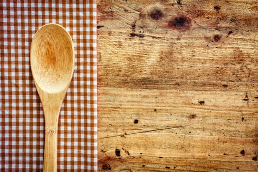 Wooden kitchen spoon on a fresh checkered rustic red and white napkin on a wooden counter with copyspace