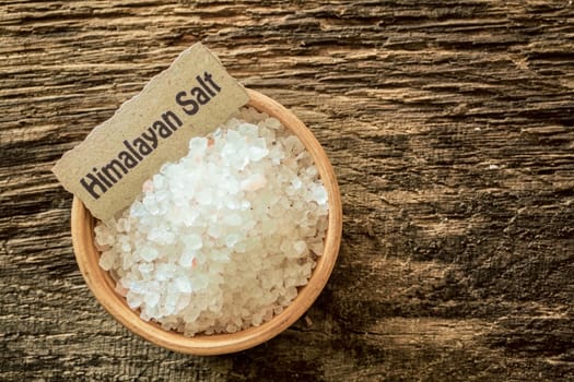 Himalayan salt crystals, a rock salt from the mines in Pakistan, in a bowl with a name label on a grunge textured wood surface, overhead view
