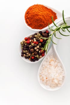 Overhead view of Himalayan rock salt, red cayenne pepper and black peppercorns in ceramic spoons with a sprig of fresh rosemary