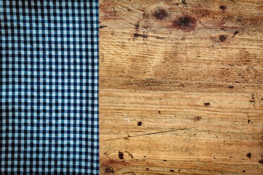 Conceptual image of a country kitchen background with an old stained wooden surface overlaid by a fresh blue and white folded napkin as a border on the left