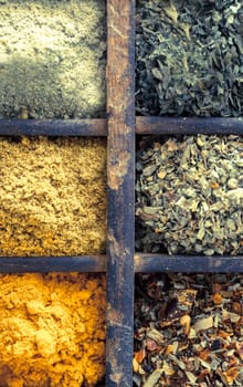 Close up overhead view of assorted dried herbs and spices in an old vintage wooden printers tray for use as seasoning and flavouring in cooking
