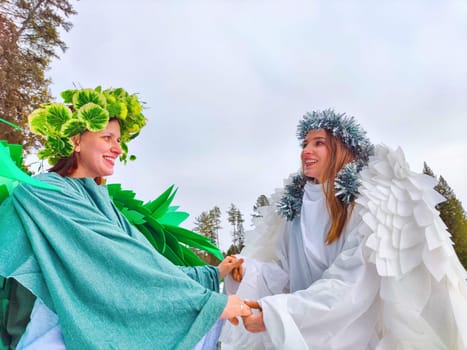 Two girls wear white and green dresses, embodying the seasons of winter and spring, while enjoying a serene moment by the lake.