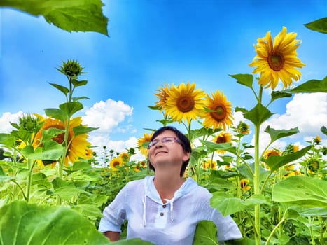 A person stands in a field of tall sunflowers, smiling gently as they soak in the beauty of nature. The sky is clear with fluffy clouds, creating a serene atmosphere.