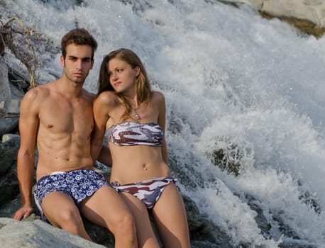 Romantic couple next to river waterfall, naked, wearing swimming suit and bikini