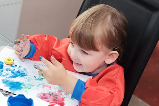 preschool girl looking at her paint covered hands and smiling
