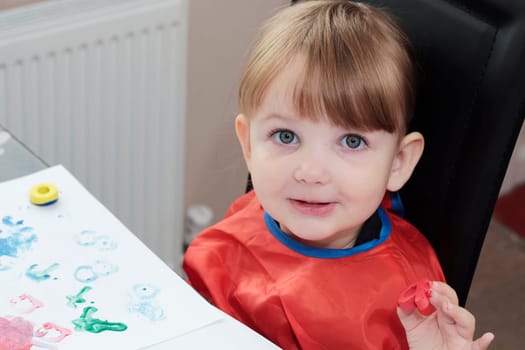 preschool girl painting a picture with foam letters, and looking directly into the camera