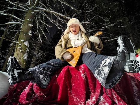 A middle-aged woman with a funny expression walks through a snowy forest at night, wearing a warm hat and playing a balalaika.