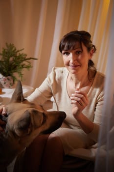 A middle-aged woman relaxes in her cozy apartment, interacting with her dog while enjoying a peaceful evening of comfort and companionship.