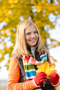 Smiling blonde teen girl autumn forest holding dry leaves