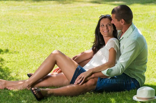 Hugging couple laughing and sitting in grass outdoors