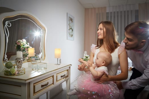 A smiling couple poses with their baby girl at a charming vanity, showcasing joy and affection in a warm and stylish setting.