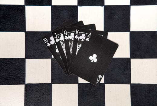 Royal flush or unbeatable winning poker hand in clubs on black cards on a chessboard viewed fanned out from overhead in a flat lay