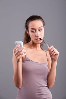 Young woman looking at her smartphone nibbling at her pen