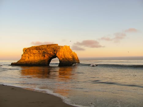 Arch rock formation on ocean beach during sunset