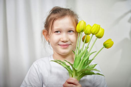 A cheerful girl with a bouquet of yellow tulips enjoys her time indoors, capturing a joyful moment in a cozy setting.