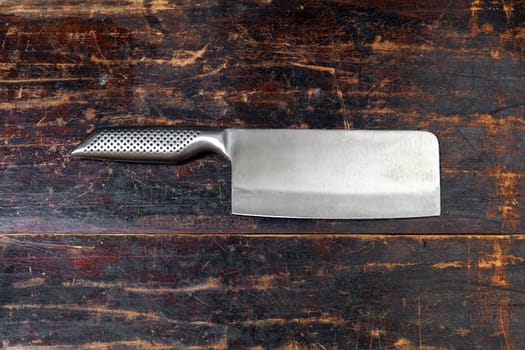 Shiny stainless steel meat cleaver with sharp blade lying on a rustic wooden board with copyspace viewed as a flat lay still life