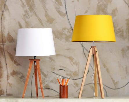 Still Life of Two Table Lamps with White and Yellow Shades on Table with Cup of Pencils in front of Patterned Background