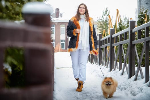 A girl walks her fluffy Pomeranian dog along a snowy path, enjoying the crisp winter air and scenic surroundings.