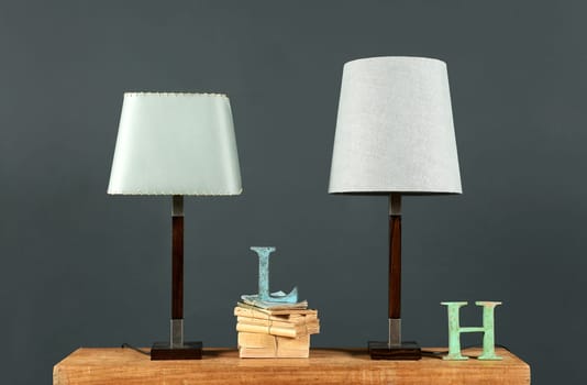 Two vintage table lamps with off white cylindrical shades on an old desk with books and metal letters against a grey wall