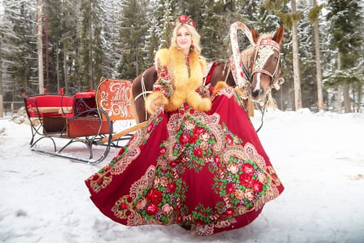 A young Russian woman in traditional attire poses with a horse during winter Maslenitsa festivities.