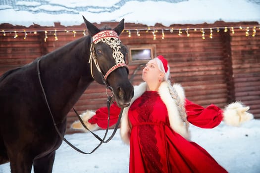 A Russian girl in traditional dress interacts with a horse, celebrating the Maslenitsa holiday in a winter setting.