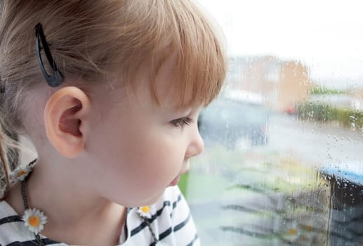 close up of a preschool girl looking out of a rain covered window