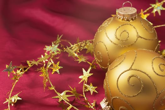 Two golden christmas bulbs with gold  chain on a red background