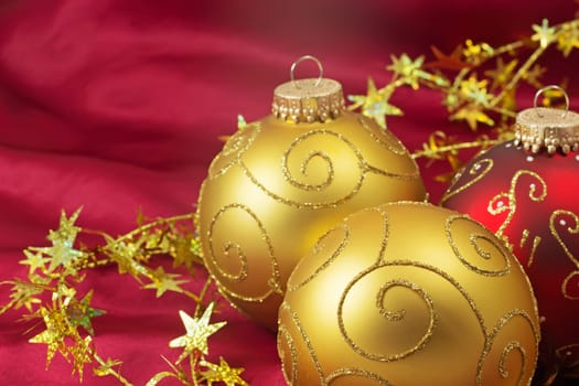 Two golden and one red christmas bulbs with gold chain on a red background