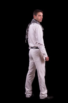View of a young urban styled fashioned man standing isolated on a black background.