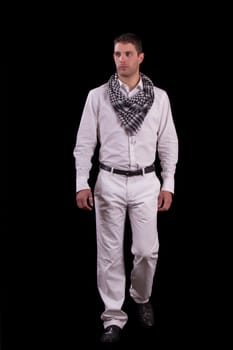 View of a young urban styled fashioned man walking isolated on a black background.