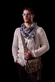 View of a young urban styled fashioned man standing isolated on a black background.