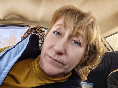 A middle-aged woman with blonde hair rests in a car while traveling, taking a break to combat fatigue during her journey.