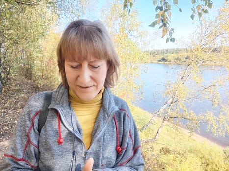 Blonde woman stands near a river surrounded by autumn foliage, capturing a moment during her outdoor adventure.