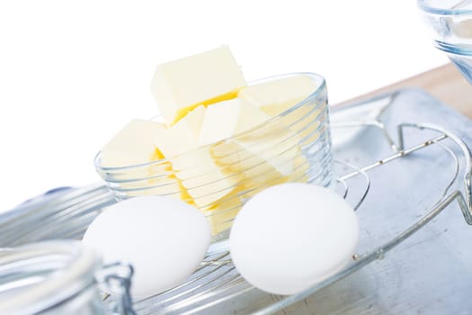 Butter in a glass bowl in front of white eggs on a cooling grid