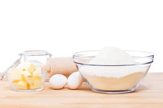 Simple baking ingredients and utensils on wooden table against a white background