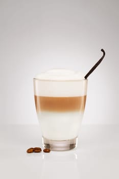 Latte macchiato with vanilla and coffee beans on grey background