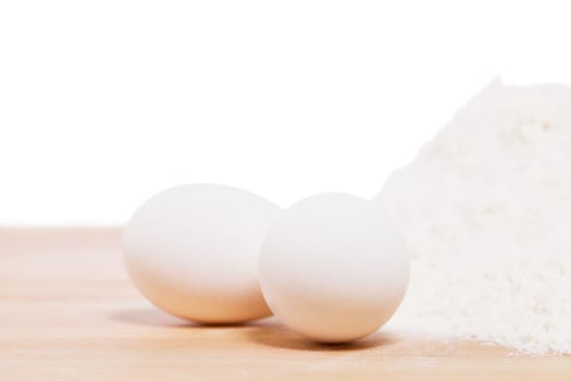 Close-up of white eggs on wood next to flour against a white background