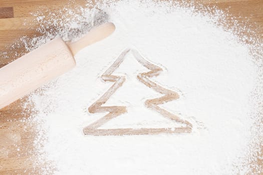 Christmas tree painted in flour next to a rolling pin on a wooden background