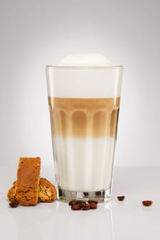 Latte macchiato with cantuccini biscuit and coffee beans on grey background