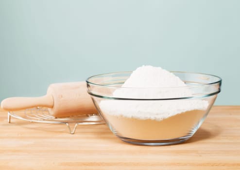 Flour in a bowl with rolling pin Danben against a green background
