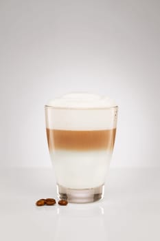 Small latte macchiato with coffee beans on grey background