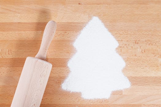 Flour in Christmas tree shape with rolling pin from above on wood