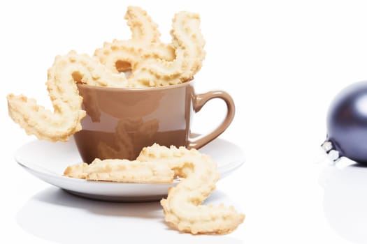 Spritz biscuits for Christmas in a cup against a white background with blue Christmas bauble