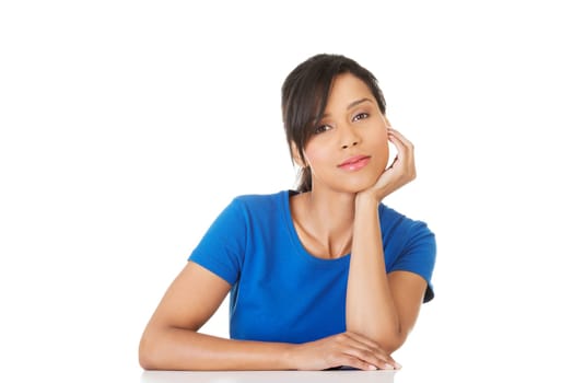 Pretty, happy, young woman in casual clothes sitting at the desk, isolated on white